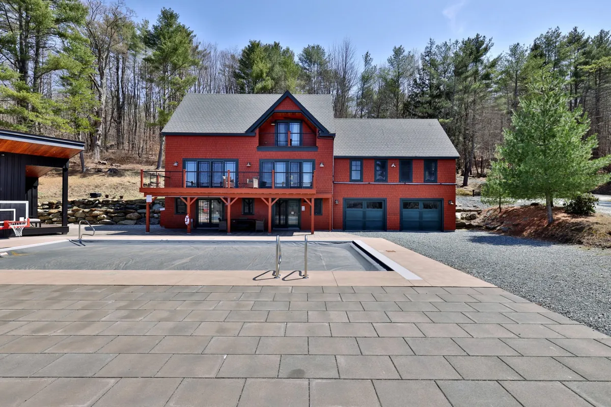 This inviting exterior shot features a red wooden house with a sparkling swimming pool in the foreground, surrounded by lush trees. The pool area is designed for private swims and cozy evenings, aligning with the section's mention of exclusive pool access for romantic evening dips. The natural setting and softly lit atmosphere evoke relaxation and exclusivity.