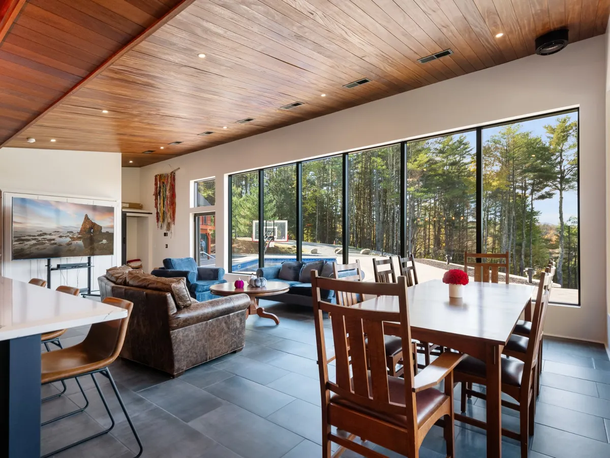 A welcoming dining area with a large table positioned beside expansive windows offering serene views of the surrounding nature. Comfortable seating and warm lighting create an ideal setting for family gatherings, sunrise coffees, or celebratory meals.