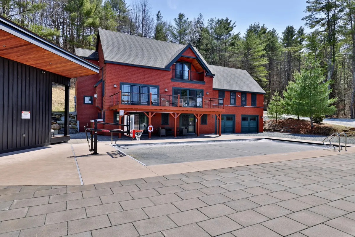 A wide-angle view of the property’s modern exterior, highlighting a pristine swimming pool and adjacent basketball area, all set against a backdrop of lush trees. The main house is visible, emphasizing both the recreational and resort-style amenities available to guests.