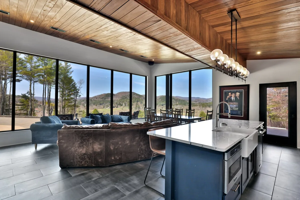 This image features a spacious open-concept living area with a modern kitchen island and comfortable seating. The large windows command breathtaking mountain views, bathing the space in natural light and highlighting the seamless connection between interior comfort and Vermont’s scenic outdoors.