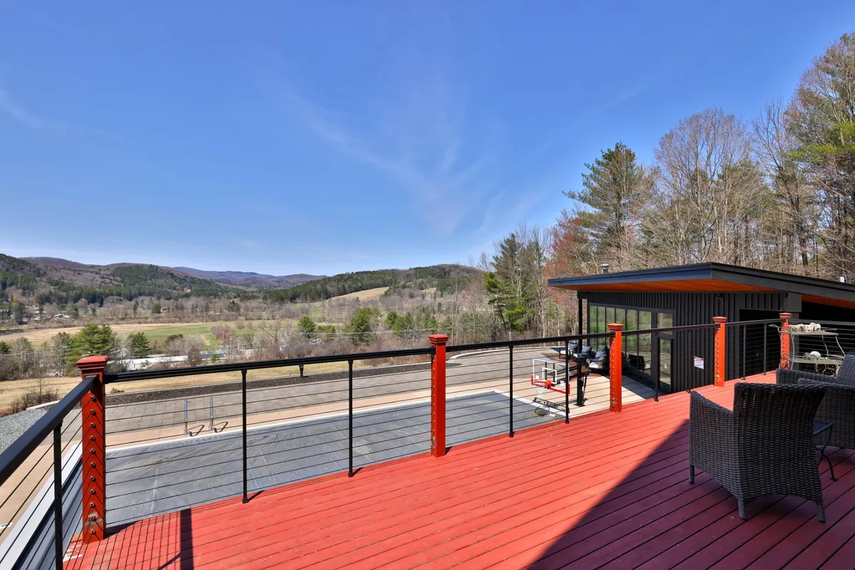 This exterior image showcases a spacious red deck with outdoor seating, set against a stunning mountain backdrop. The view stretches to the distant peaks, promising both privacy and awe-inspiring natural beauty. The deck is ideal for relaxing with a morning coffee or sharing a romantic sunset meal, while the surrounding trees enhance the secluded, tranquil atmosphere.