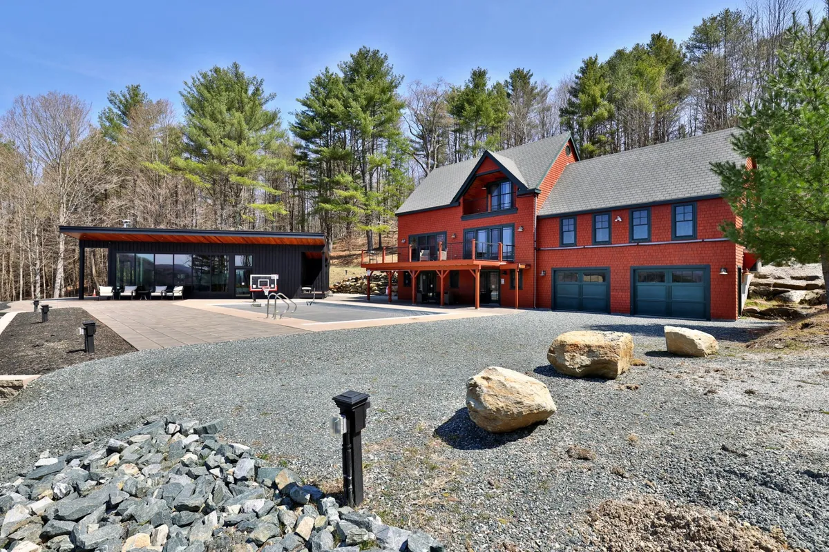 A dynamic exterior showing a red brick house paired with a sleek modern black structure, featuring an outdoor basketball court, large boulders, and thoughtfully landscaped areas ideal for gatherings.