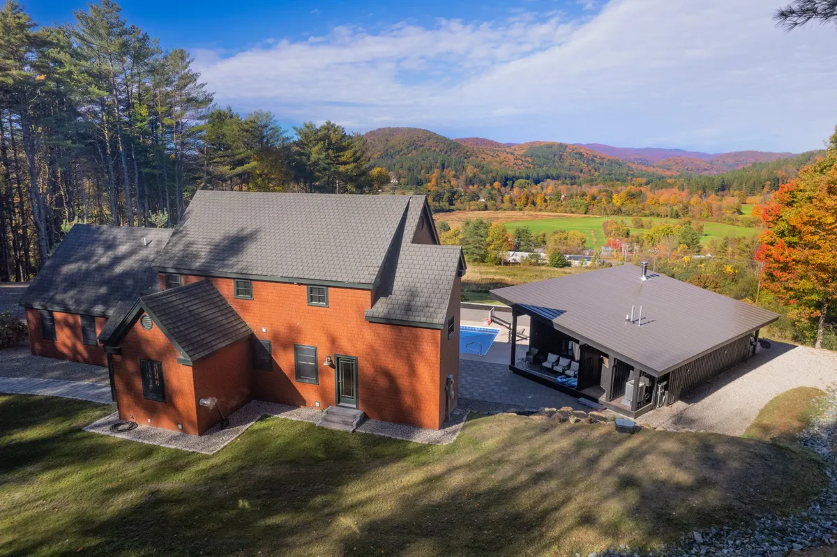 A wide view showing both the main house and the pool house set around the swimming pool, with lush landscaping and scenic surroundings. The layout emphasizes the spaciousness and privacy of the estate, ideal for group gatherings and family celebrations.