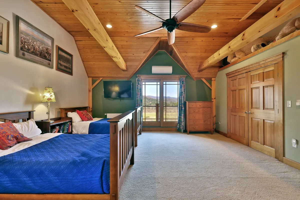 A cozy bedroom with wooden beds, large windows offering stunning mountain views, a ceiling fan, and tasteful artwork. The space feels peaceful and is well-suited for restful nights or leisurely mornings.