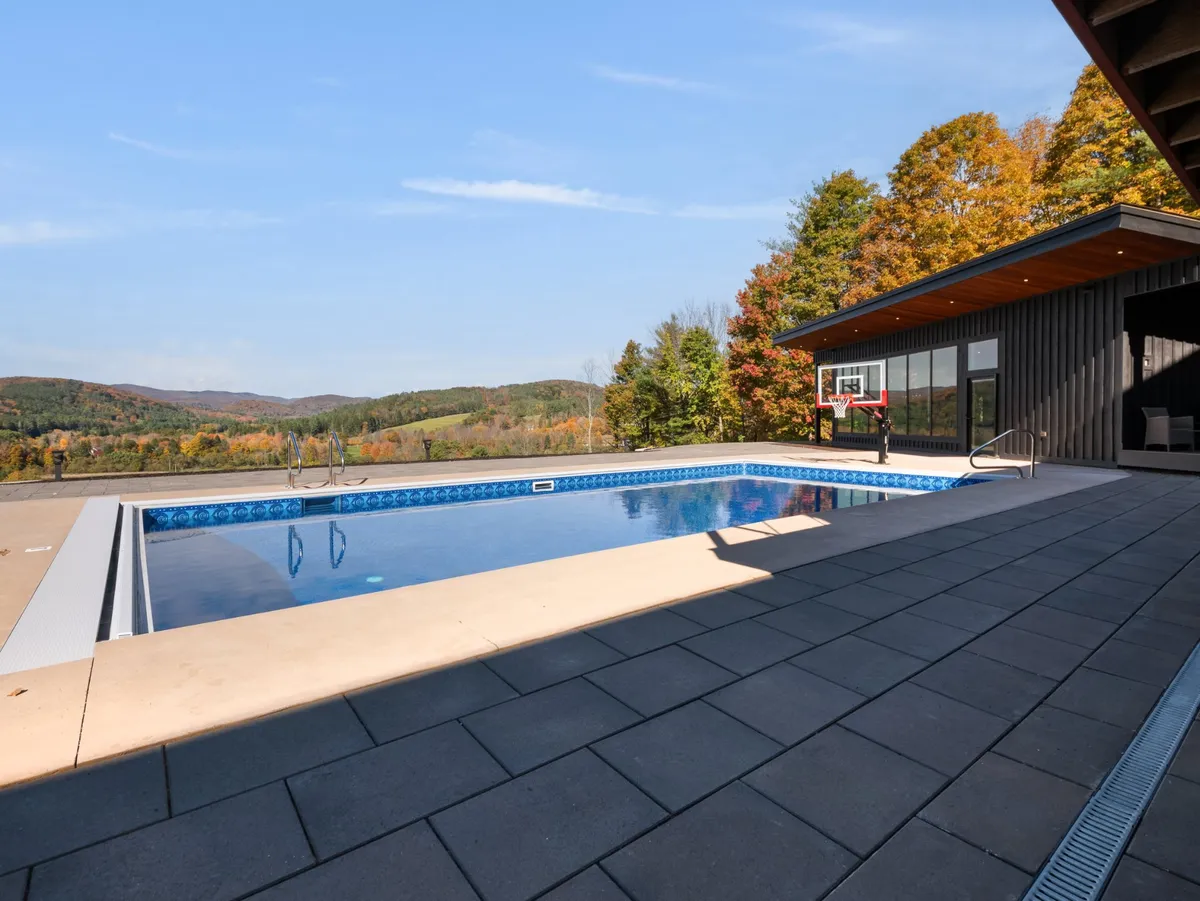 This exterior image showcases the resort-style swimming pool against the backdrop of modern architecture. The pool is complemented by a visible basketball hoop and attractive lounge areas, emphasizing recreation and relaxation. The surrounding landscape suggests privacy and tranquility, ideal for a private aquatic oasis.