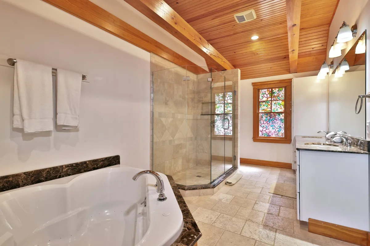 A luxurious bathroom with a deep soaking tub, glass shower enclosure, stained glass window, and a granite countertop vanity. The space is filled with natural light, creating a spa-like atmosphere perfect for relaxation and self-care.