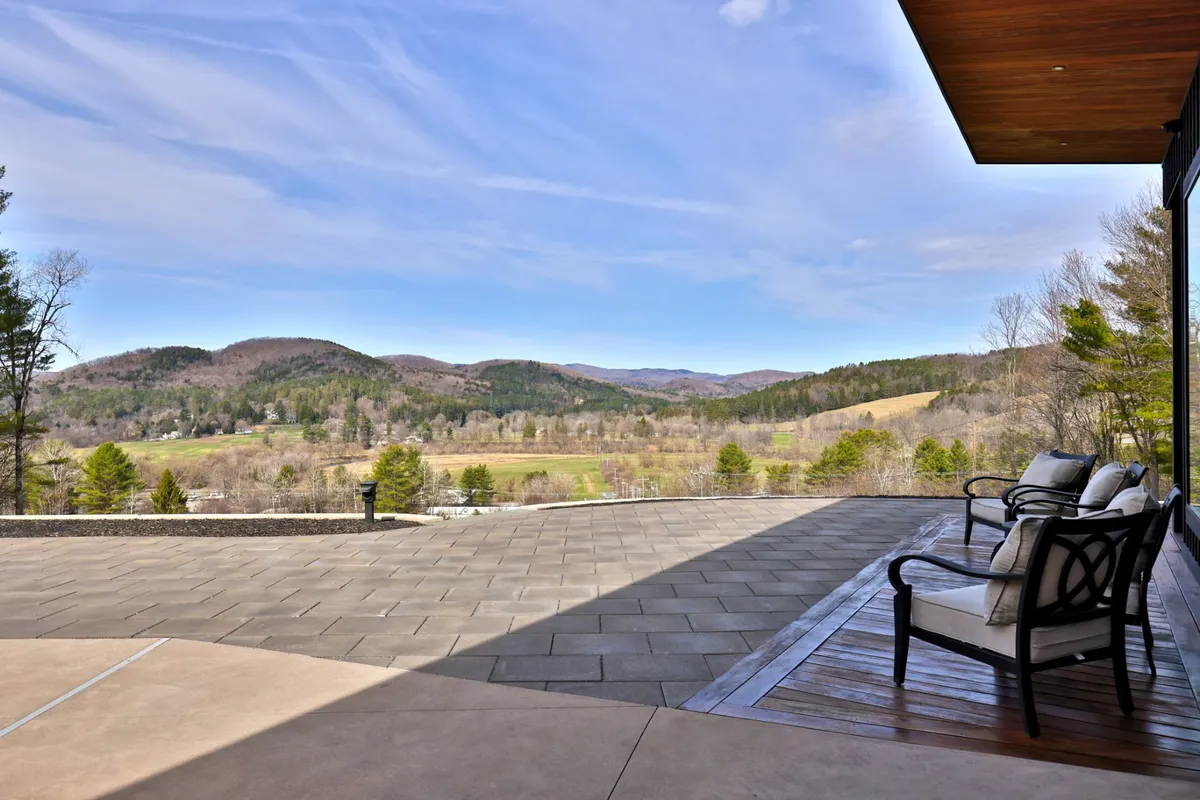 A serene outdoor scene with a spacious patio, comfortable seating, and sweeping views of a mountain range. The setting is calm and inviting, ideal for relaxing after a day of skiing, golfing, or other outdoor adventures, while offering a direct connection to Vermont's natural beauty.
