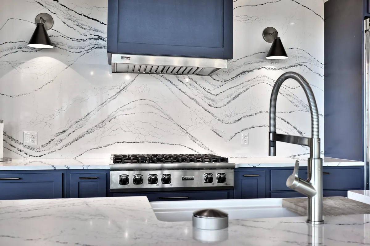 A sophisticated kitchen interior with marble countertops, blue cabinetry, and high-end stainless steel appliances. The space is styled for gourmet cooking and entertaining, aligning well with the mention of a custom Viking kitchen.